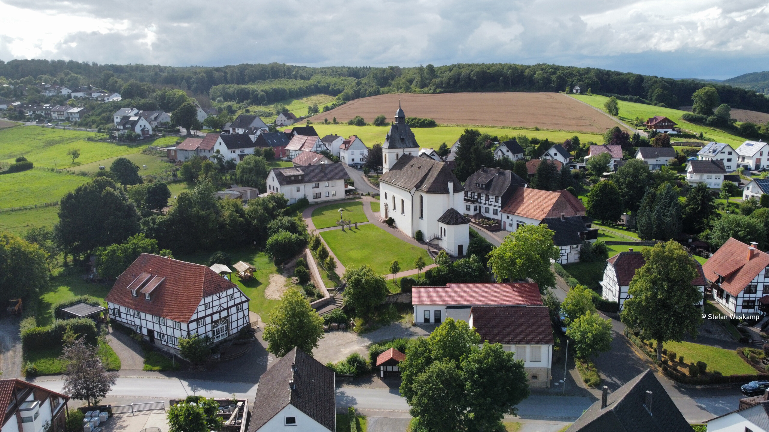 Ein Dorf das auf einem grünen Hügel liegt. Häuser, Bäume und eine Kirche